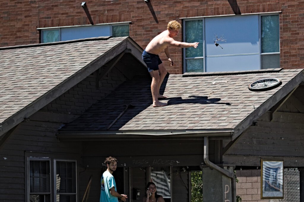 A man cleaning off a round of Toss Shit on the Roof from his rental house's roof during Purdue's Grand Prix weekend